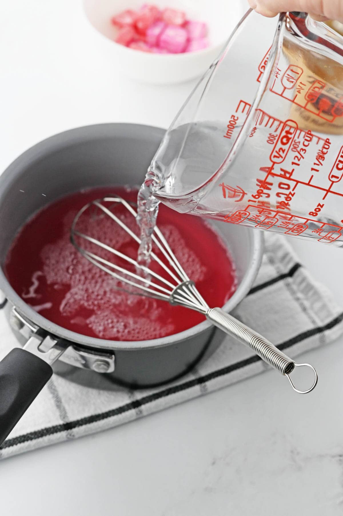 A person pouring clear liquid into a pan with a whisk.