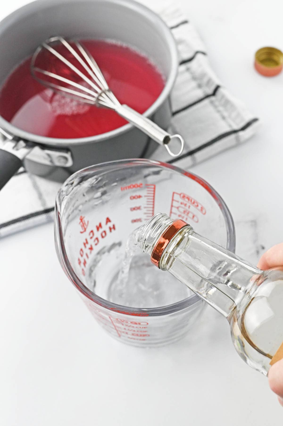 A person pouring clear liquid into a measuring cup.