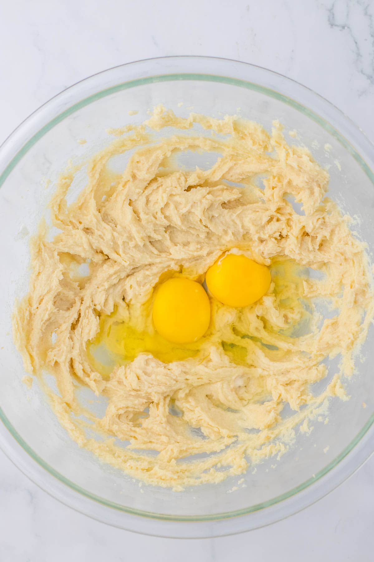Two eggs with batter in a glass bowl.