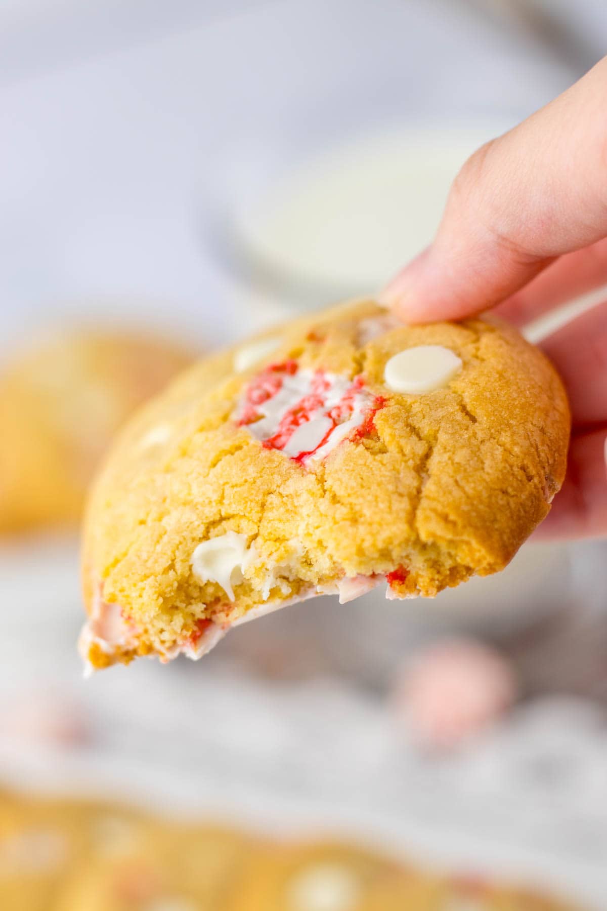 A hand holding a cookie with peppermint and white chocolate chips.