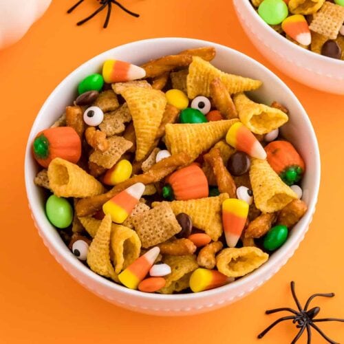 Halloween chex mix in bowls on an orange background.