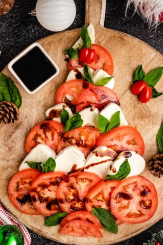 A christmas tree with tomatoes, mozzarella and basil on a wooden cutting board.