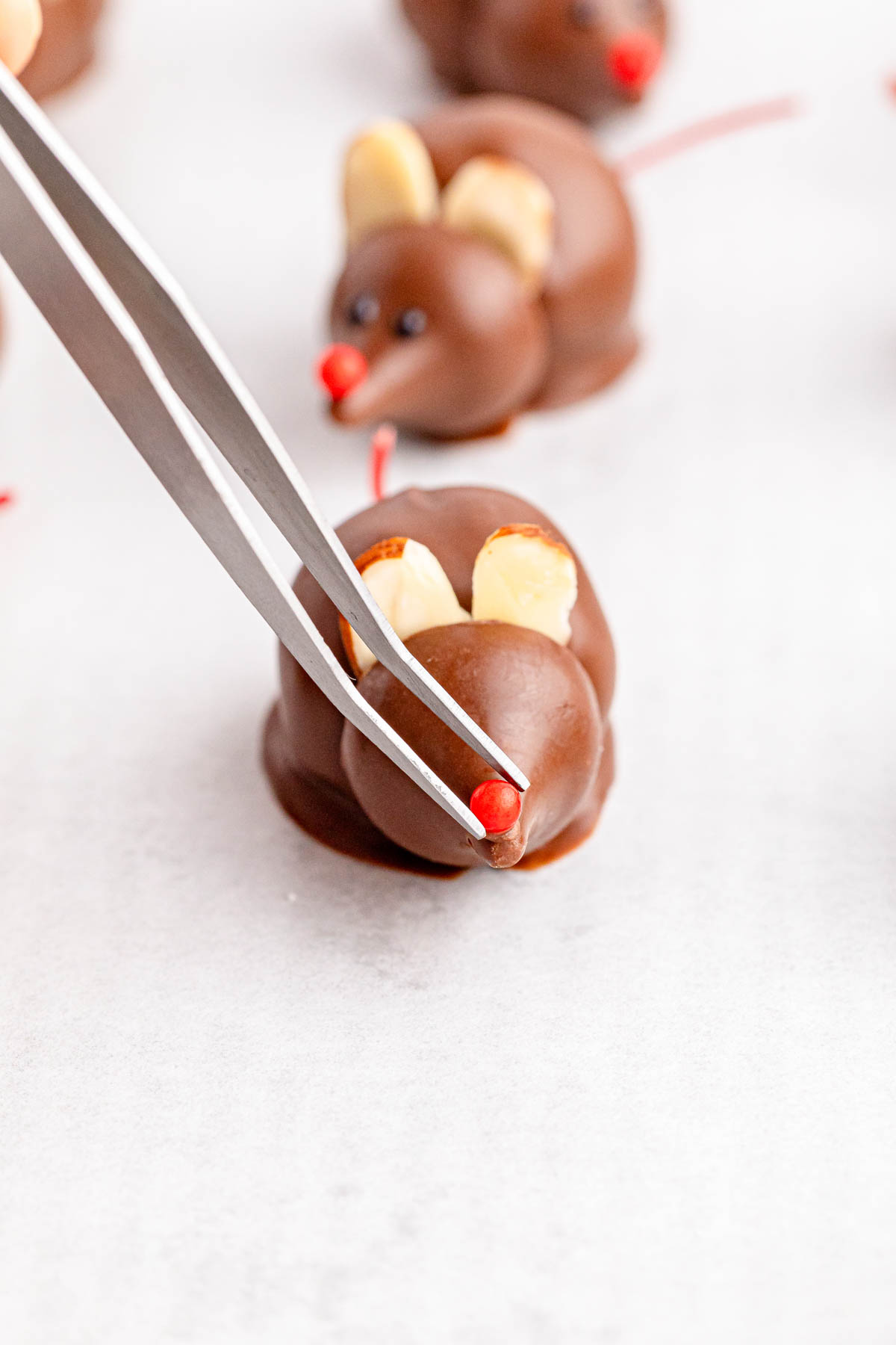 A person putting the nose on a chocolate mouse with tweezers