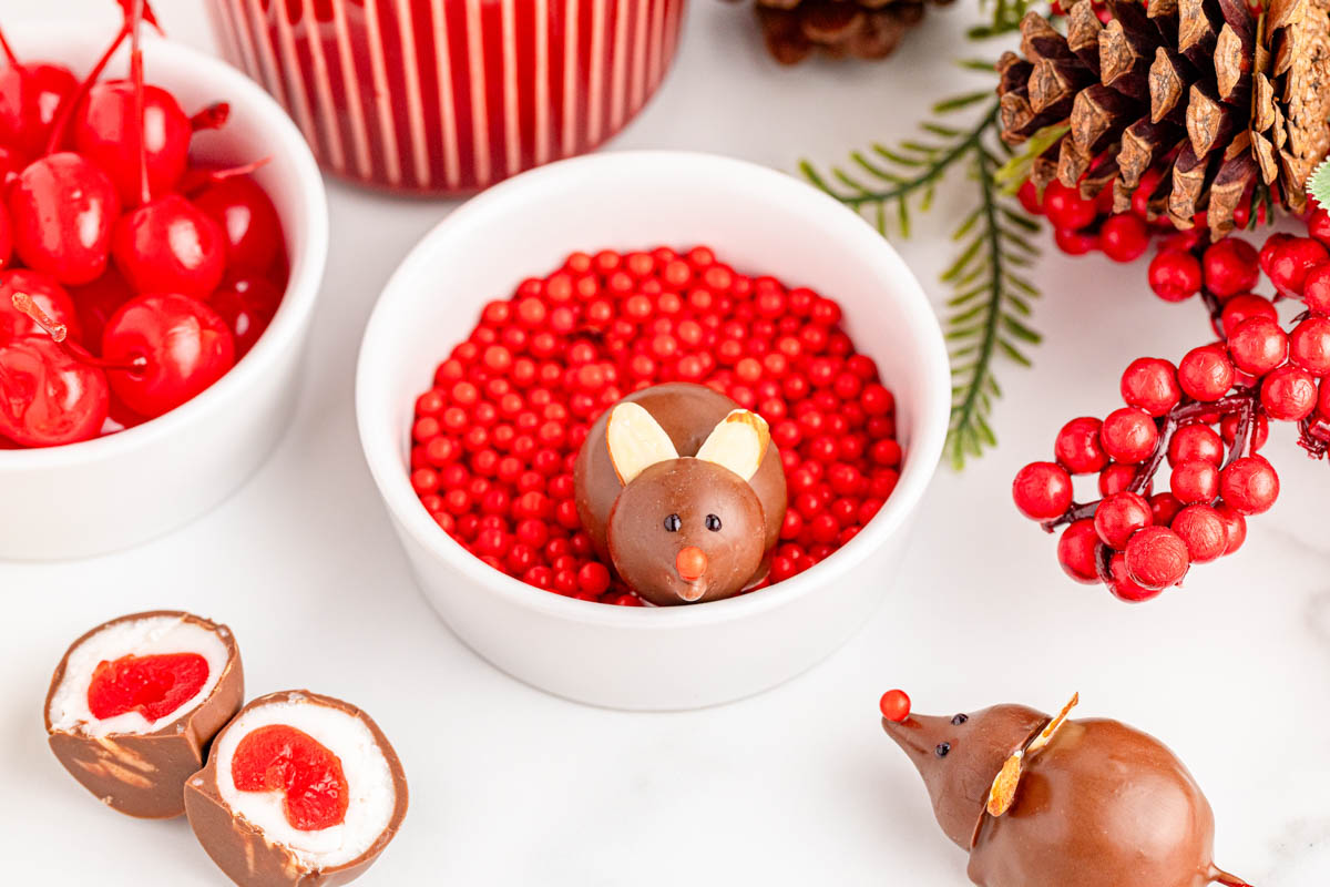 A bowl of chocolates with a mouse and red cherries.