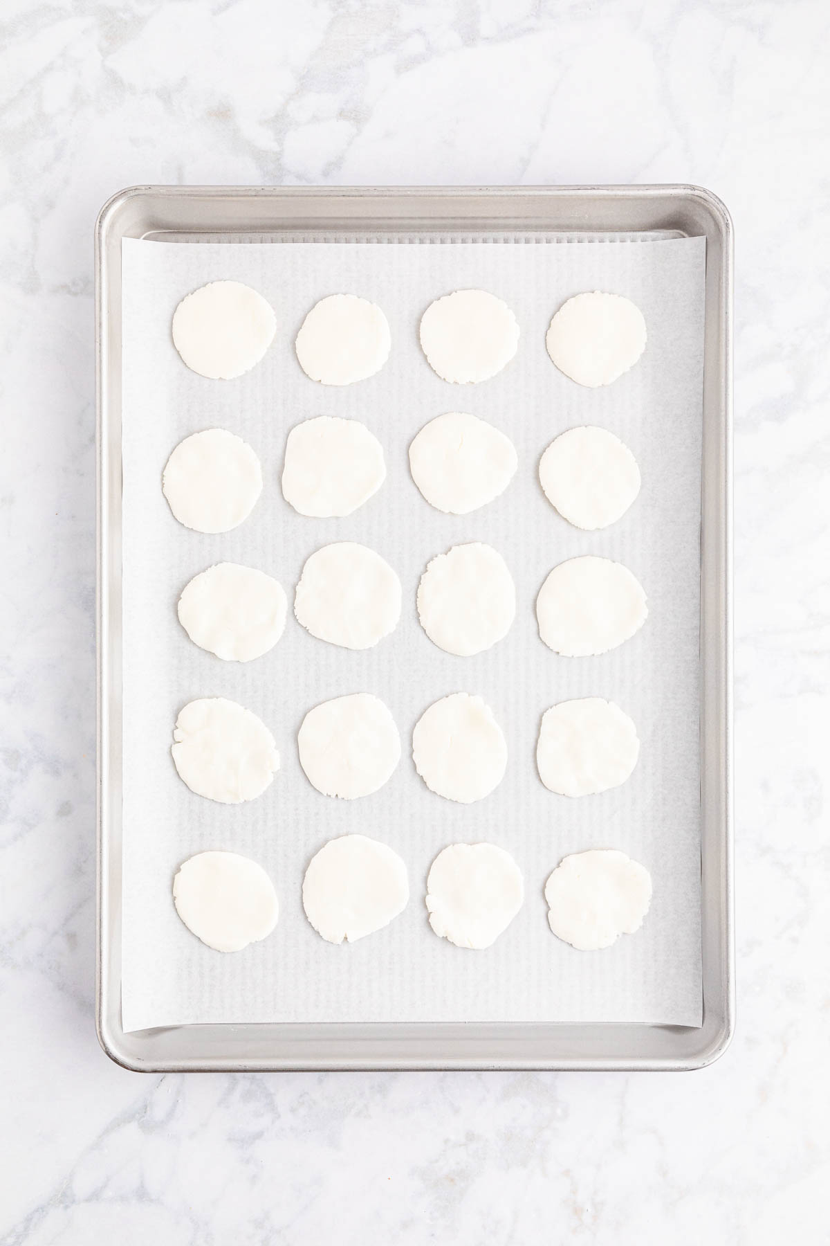 White sugar circles on a baking sheet on a marble countertop.