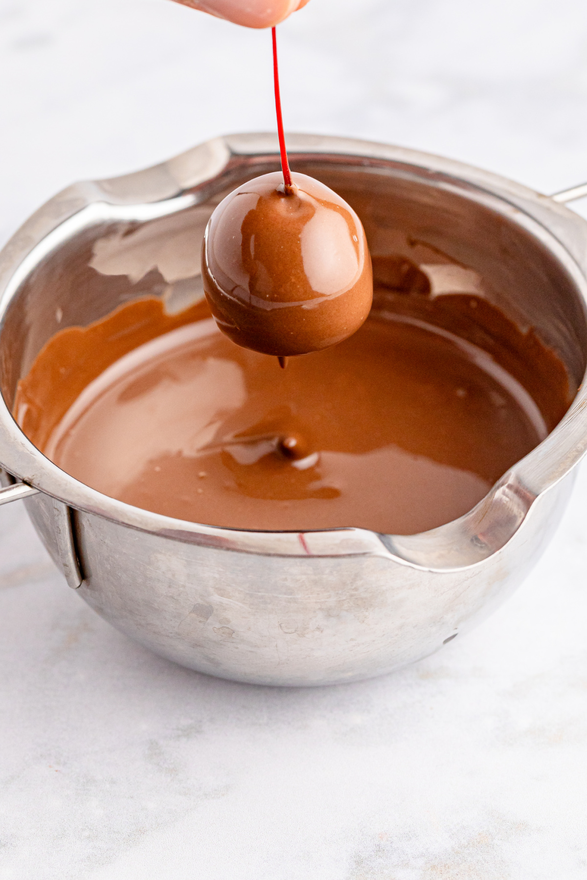A person is holding a chocolate covered cherry over a pan.