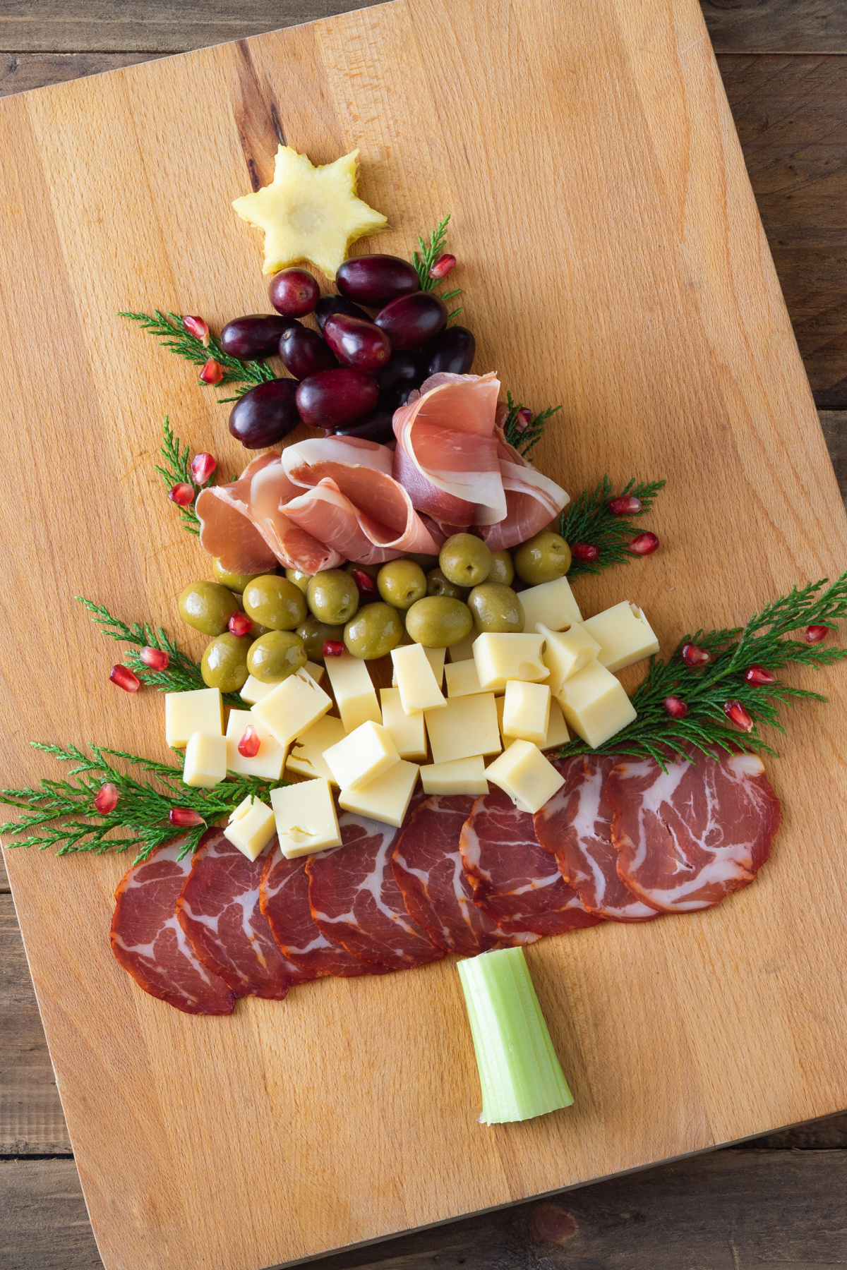 A wooden cutting board with a christmas tree made of meats and olives.