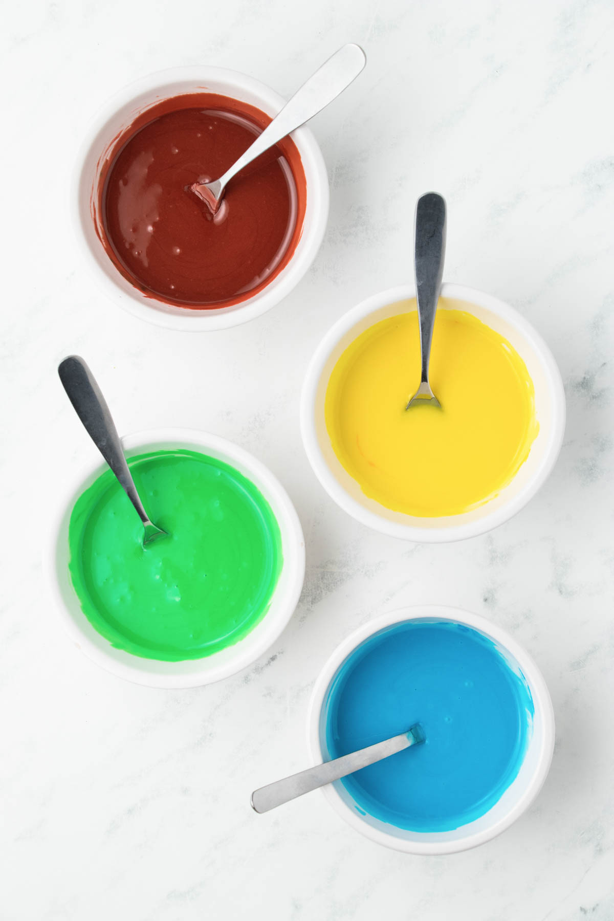 Four bowls with different colors of icing in them.
