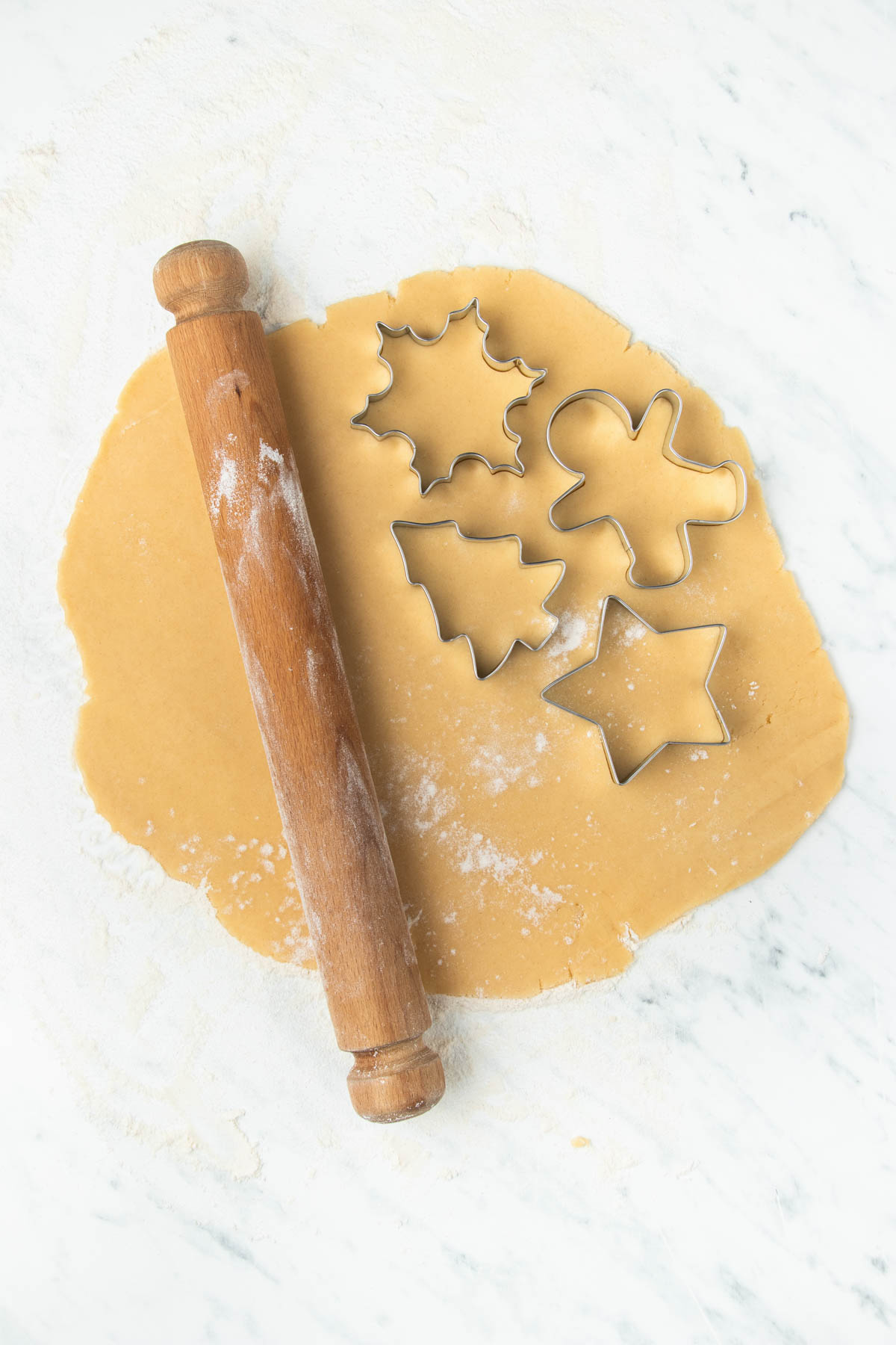 Gingerbread cookie cutter and rolling pin on a marble countertop.