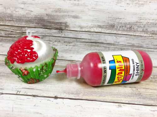 A cupcake ornament next to a bottle of paint.