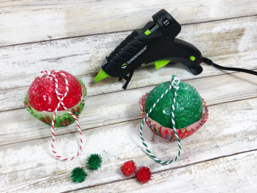 Two christmas ornaments with a glue gun next to them.