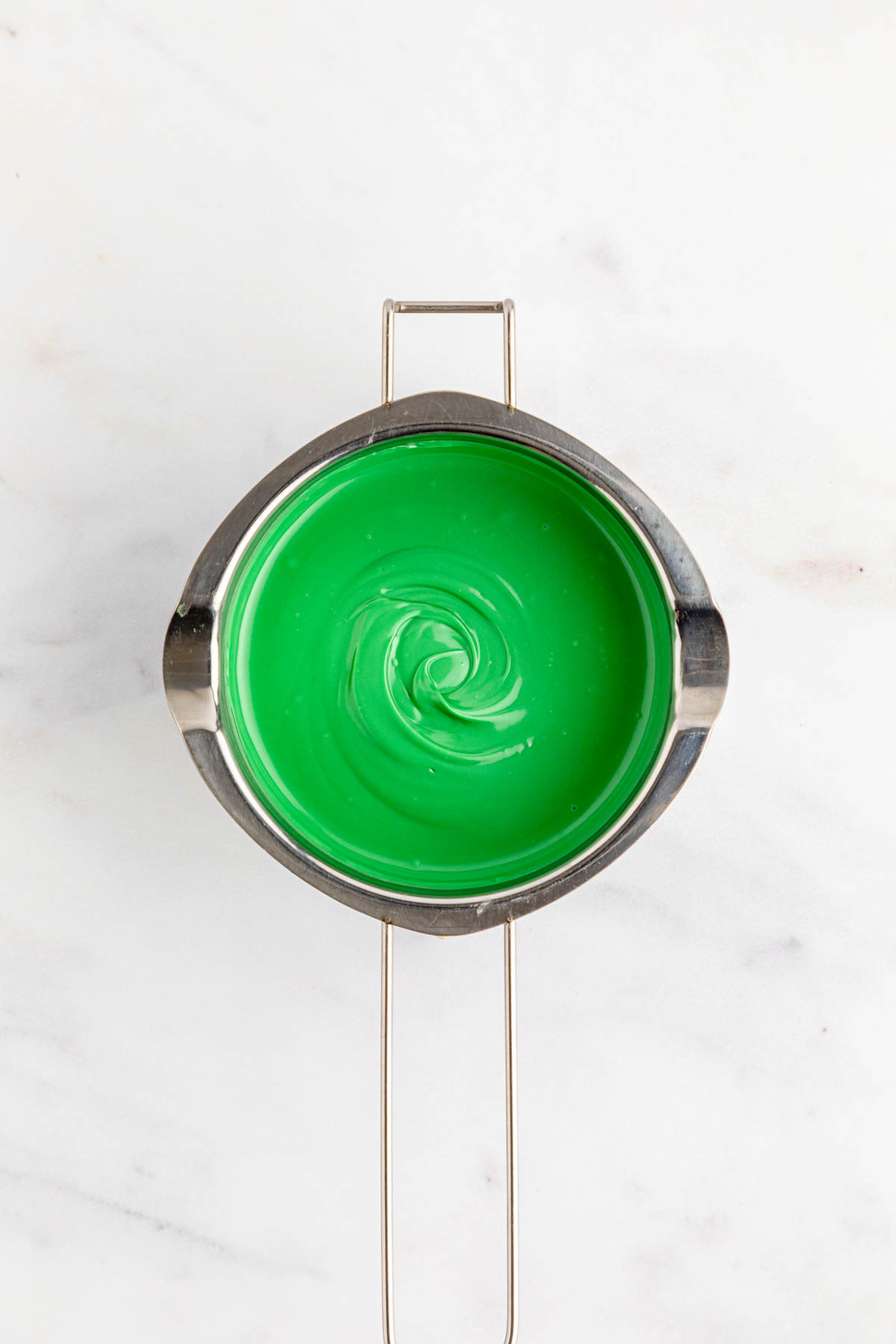 Green melted chocolate in a pan on a marble countertop.