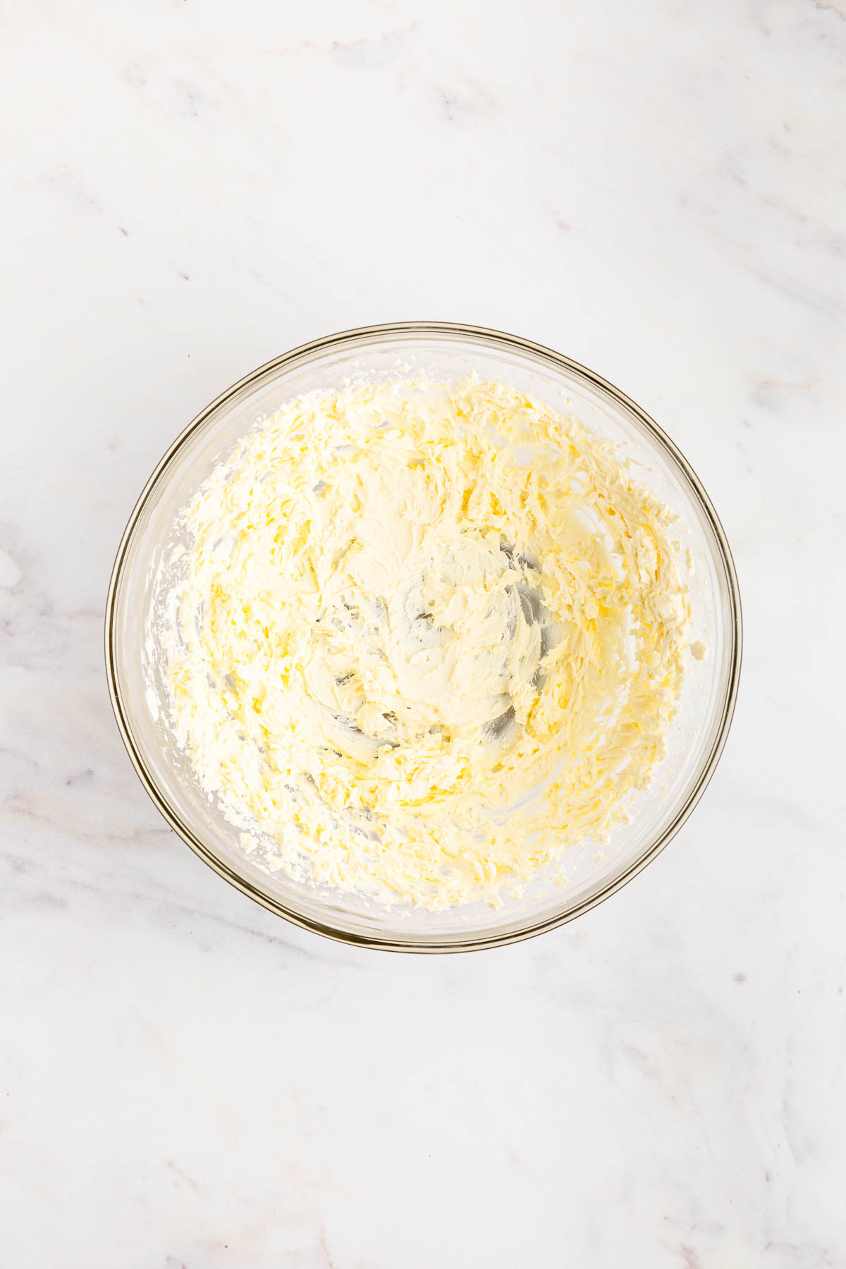 Cream cheese in a glass bowl on a marble surface.