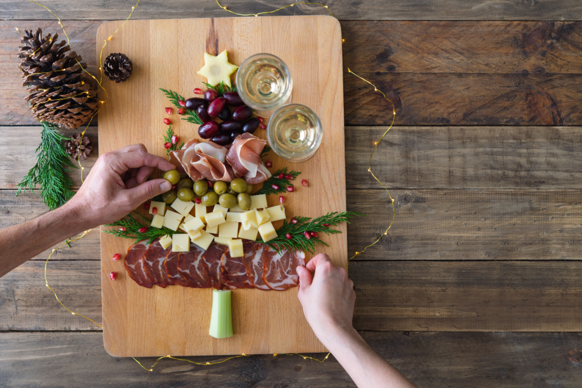 A person is preparing a christmas tree with cheese and meats on a wooden cutting board.