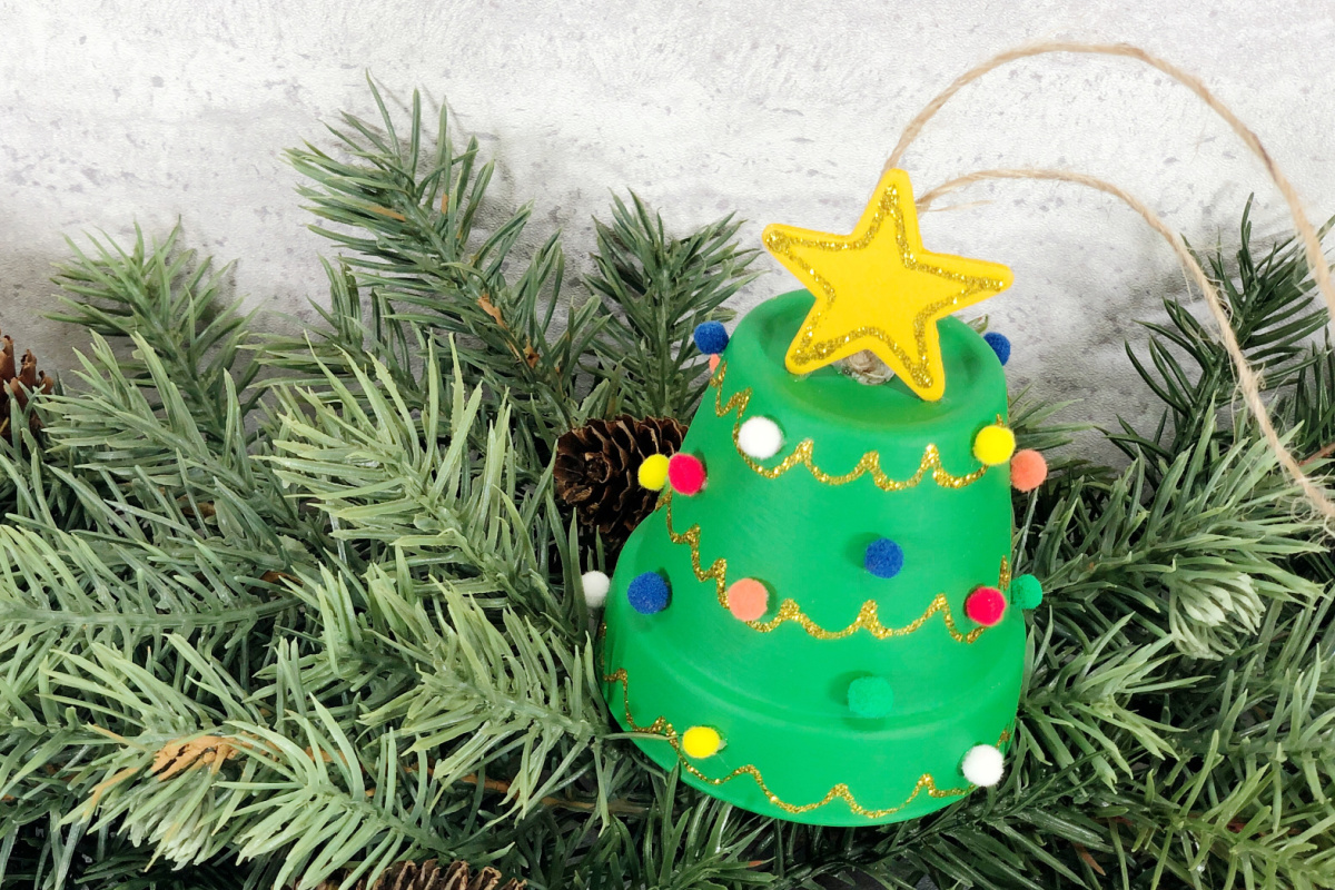A green christmas tree ornament hanging from a pine tree.