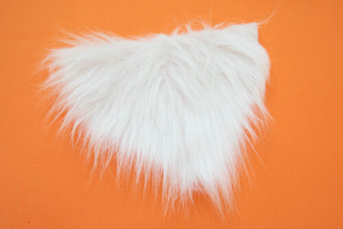 A white furry piece of craft fur on an orange surface.