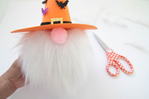 A person is holding a gnome pumpkin with a pair of scissors.