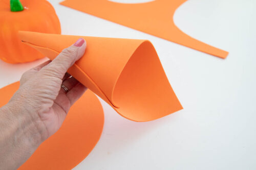 A person cutting out orange craft foam to make a witches hat