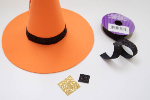 A witch hat with ribbon and glitter cardstock on a table.
