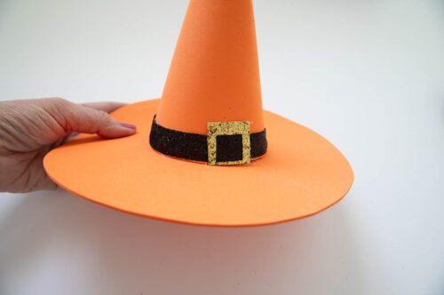 A person holding an orange witch hat with a gold buckle.