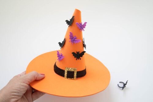 A person holding an orange witch hat with bats on it.