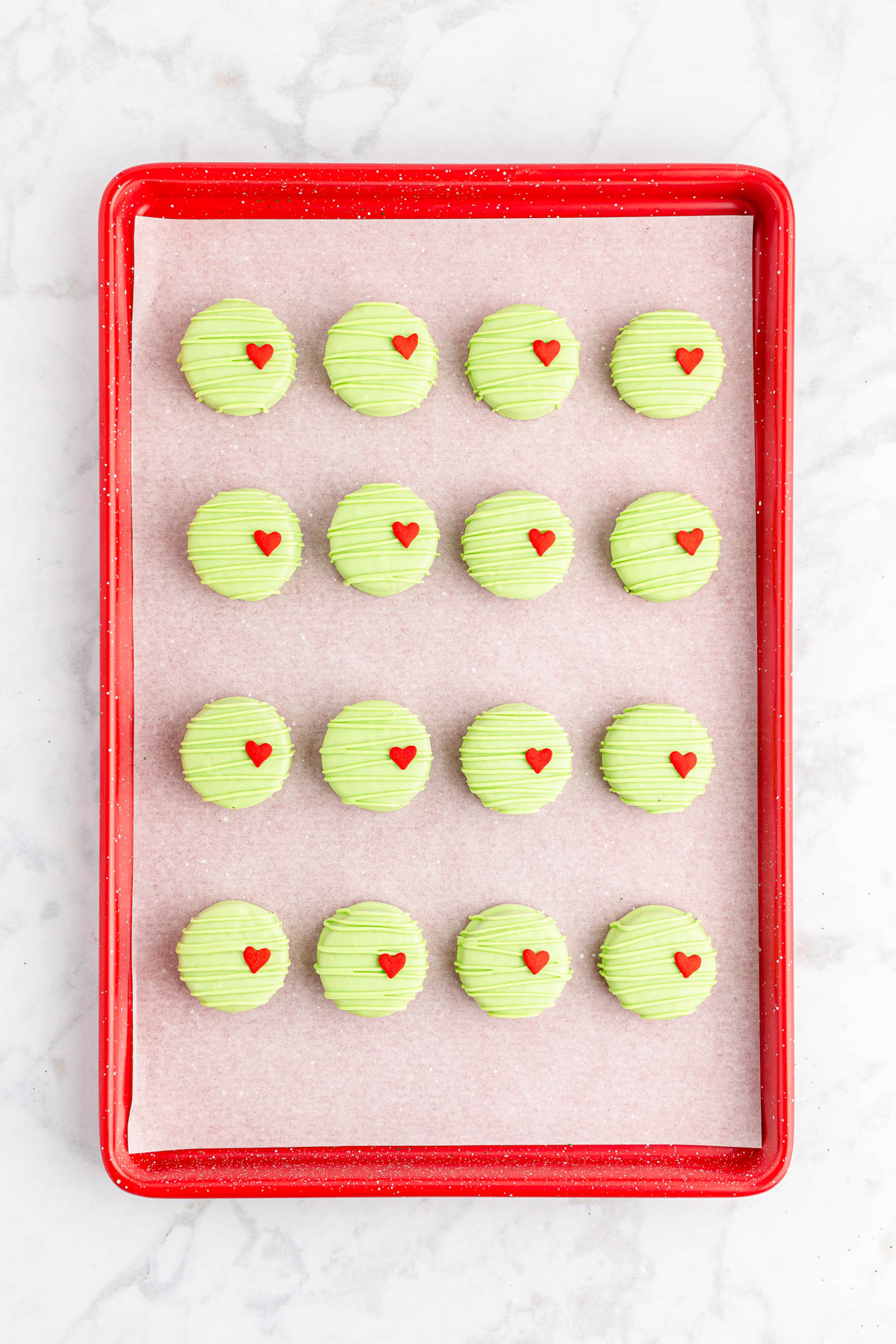 A tray of green cookies with heart shapes on a marble countertop.