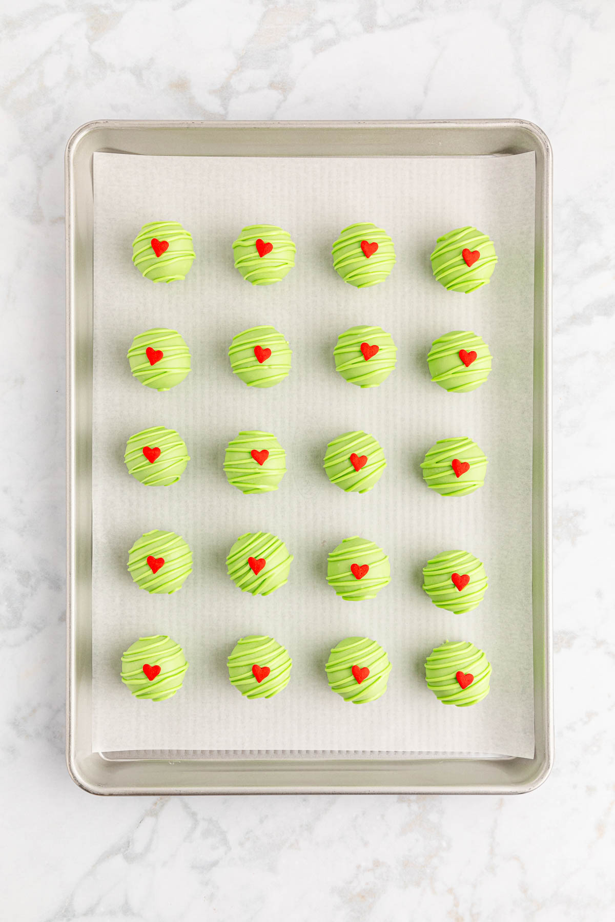Green heart decorated Oreo balls on a baking sheet.