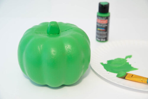 A green pumpkin with paint on a plate next to a paint brush.