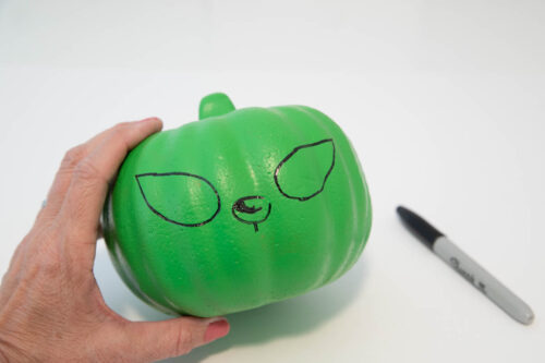 A hand holding a green pumpkin with a face drawn on it.
