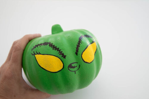 A person holding a green pumpkin with eyes painted on it.