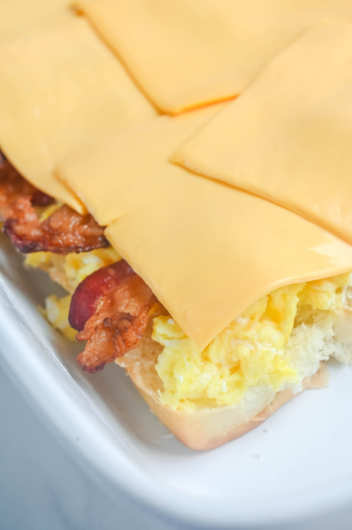 Breakfast sandwich with bacon and cheese on a white plate.