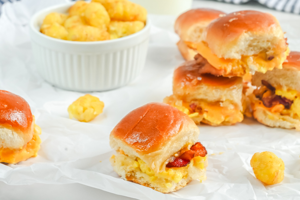 Bacon, egg and cheese slider on white paper with sliders piled behind