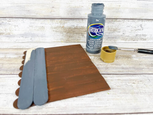 A bottle of paint and a paint brush on a wooden surface.