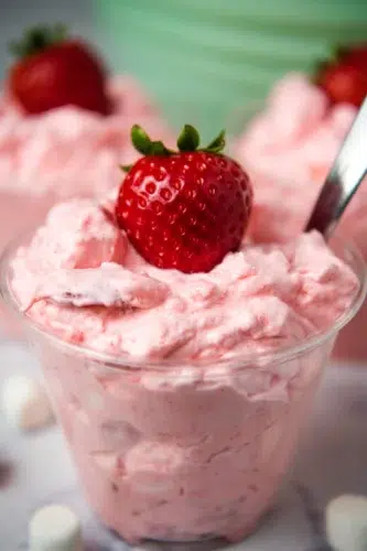 A bowl of strawberry ice cream with strawberries and marshmallows.