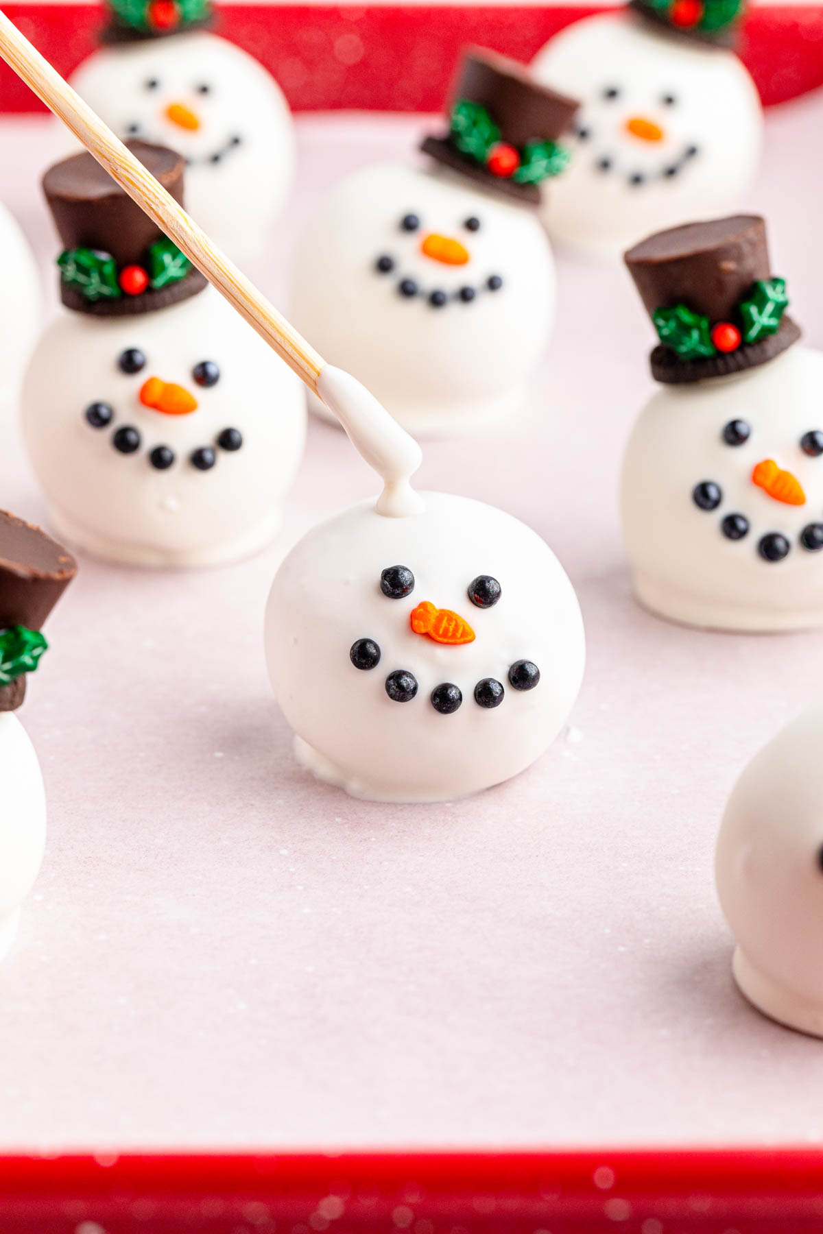 Snowman Oreo balls on a tray with a stick dipped in chocolate in the middle.