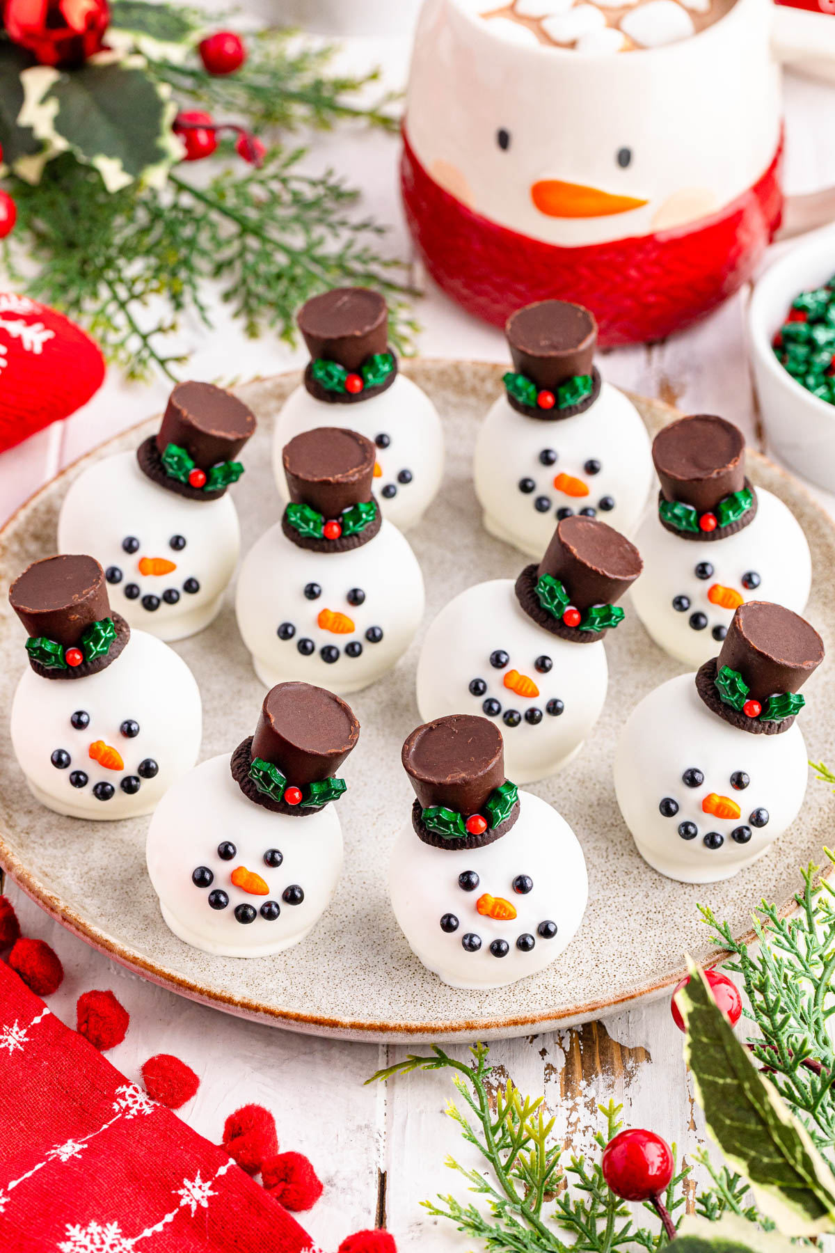 Snowman oreo balls on a plate with a cup of hot cocoa.