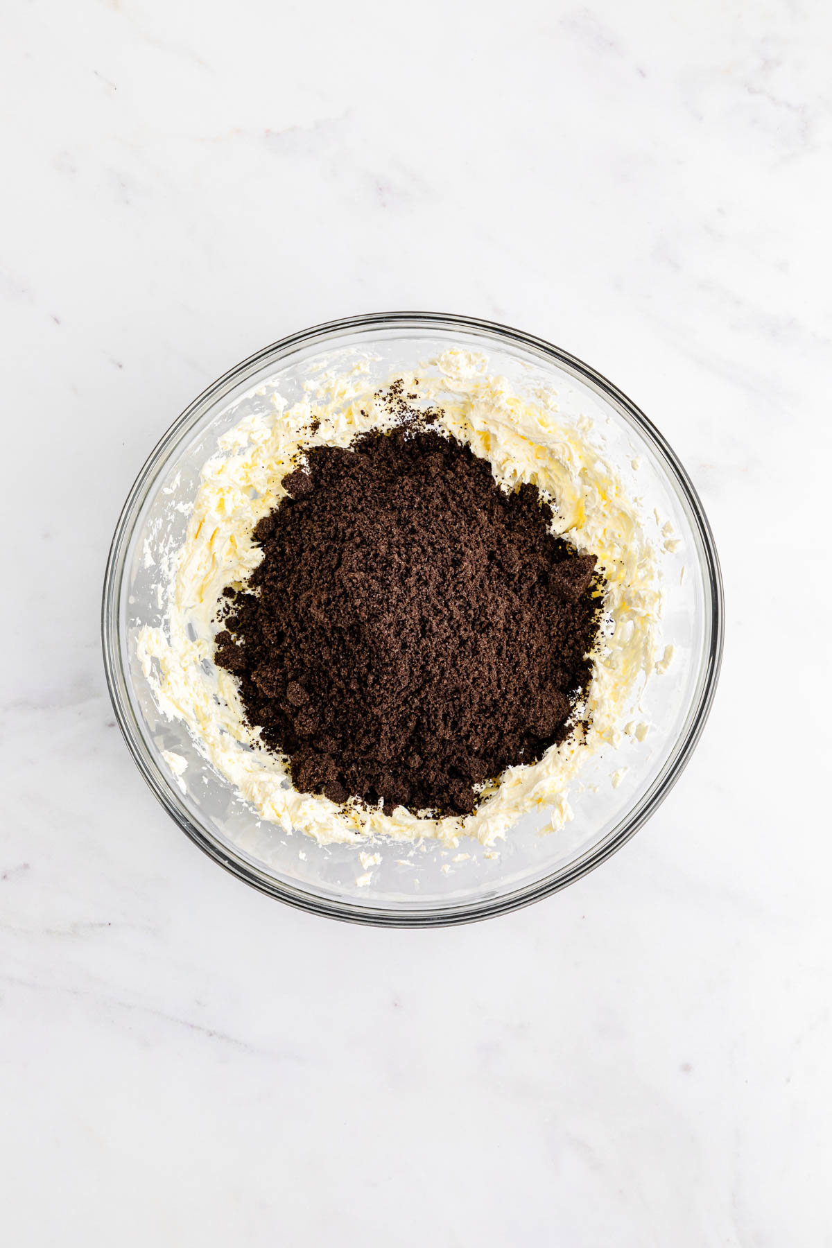 A glass bowl filled with a mixture of cream cheese and Oreo crumbs