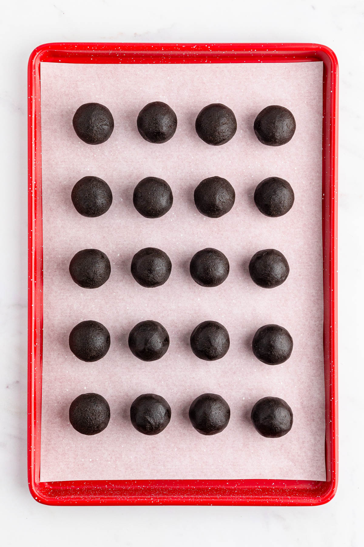 Chocolate truffles in a red tray on a marble counter.