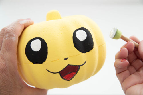A person is holding a yellow pumpkin with a round sponge brush in the other hand