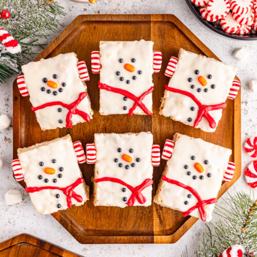 Snowman rice krispie treats on a cutting board with peppermint candies