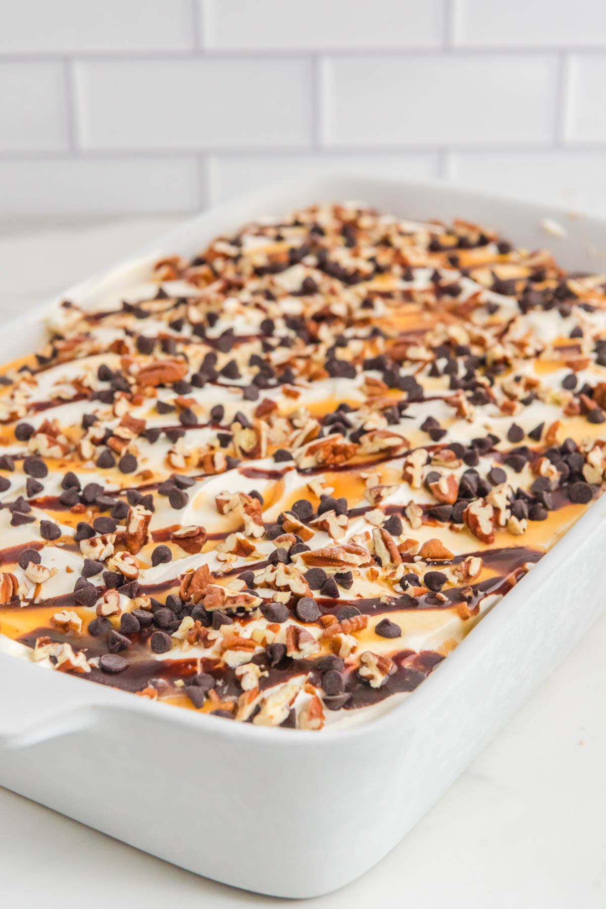 An ice cream cake with chocolate and pecans on top.