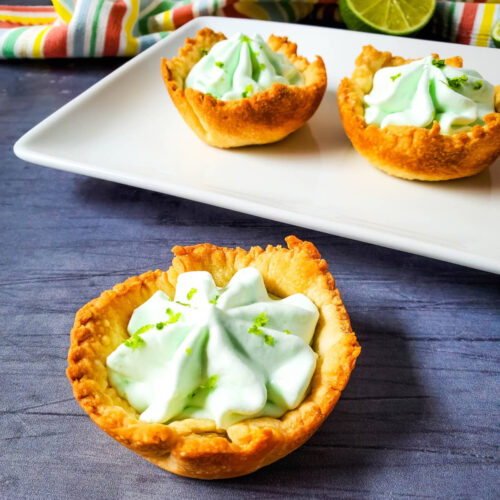 Lime tarts on a plate with lime wedges.