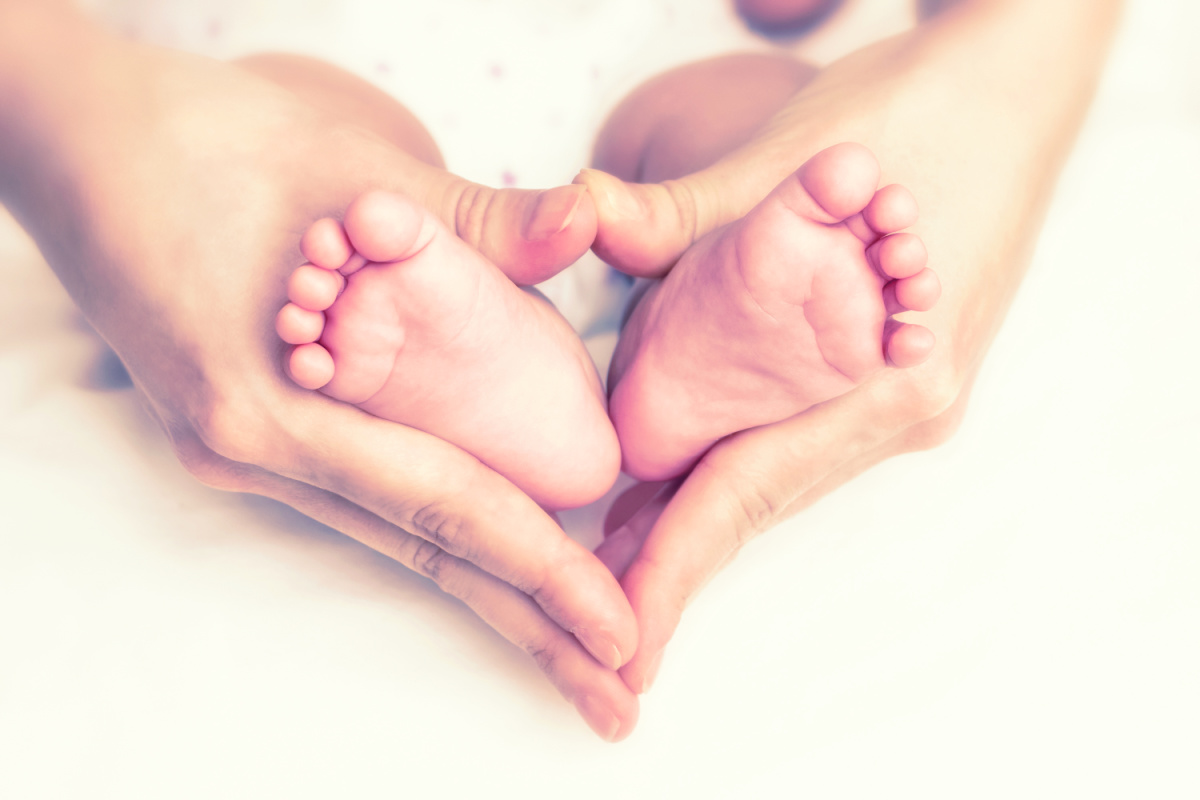 A woman's hands are holding a baby's feet in a heart shape.