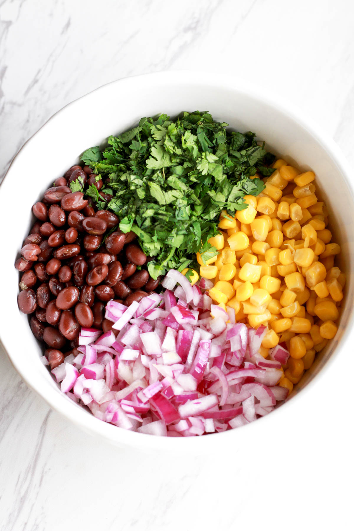 Ingredients for bean and corn salsa in a white bowl.