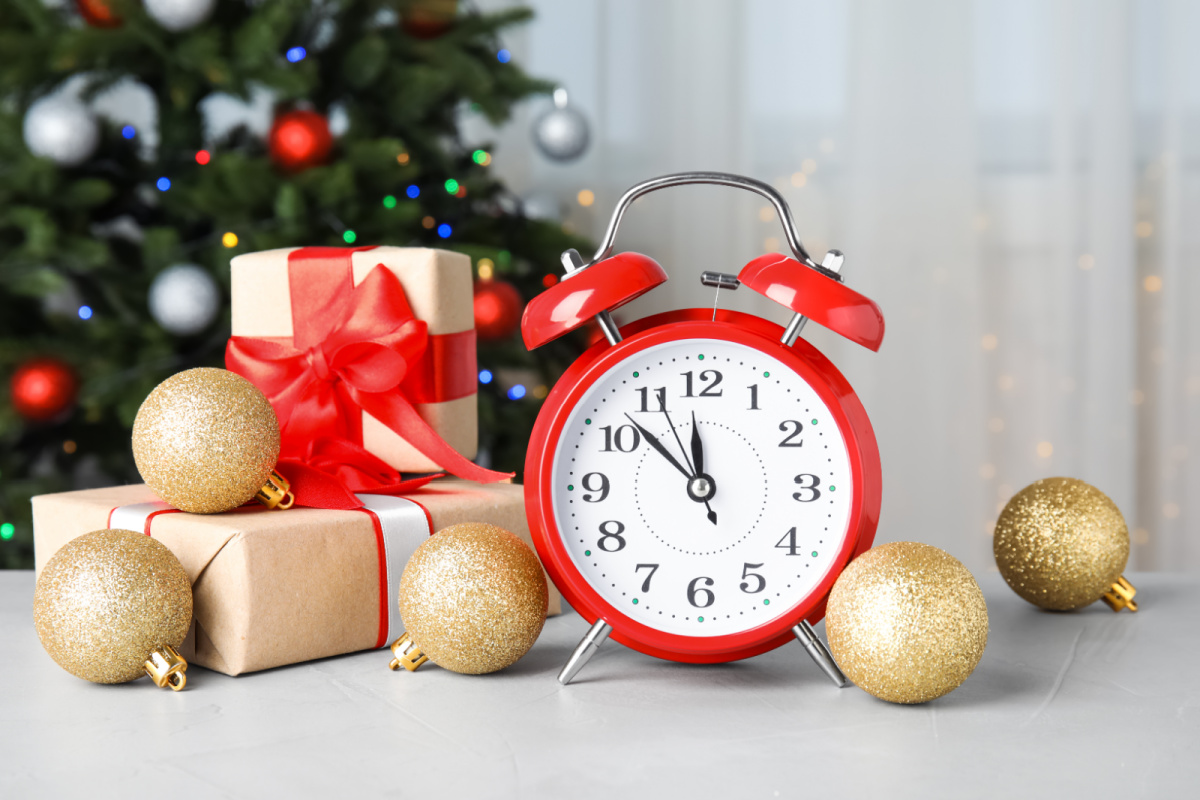 A red alarm clock next to a christmas tree and gold balls.