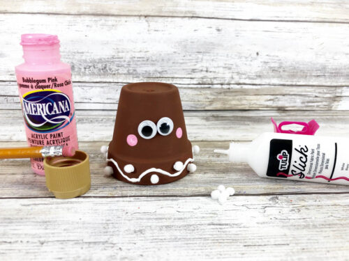 A gingerbread clay pot craft with a bottle of paint and a bottle of glue.