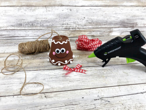 A glue gun is next to a string and a gingerbread ornament.