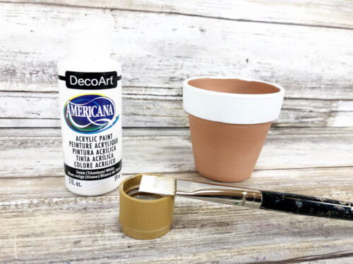 A bottle of paint and a brush next to a pot.