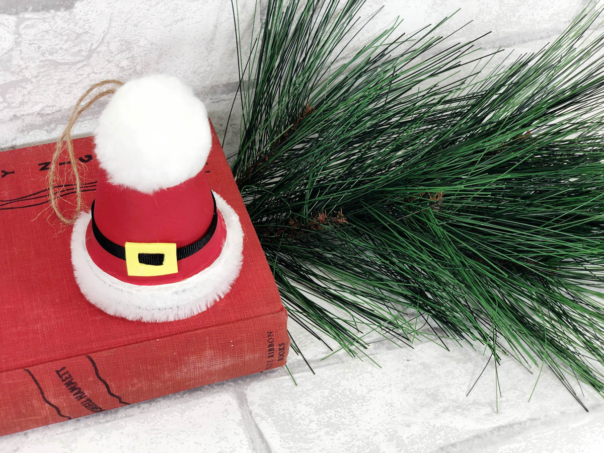 A red santa hat ornament is sitting on top of a book.