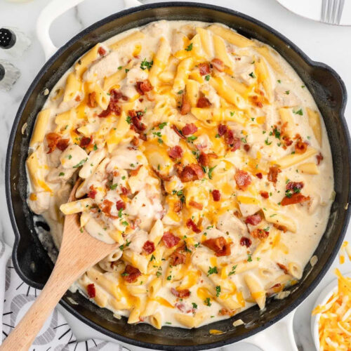 A skillet filled with pasta and cheese with a wooden spoon.